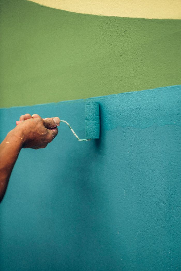 services-02 A person using a roller brush to paint a wall with blue and green colors, capturing a renovation moment.
