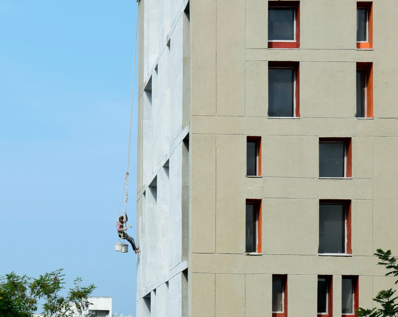 services-03 A painter suspended on a building facade, painting a high-rise structure.