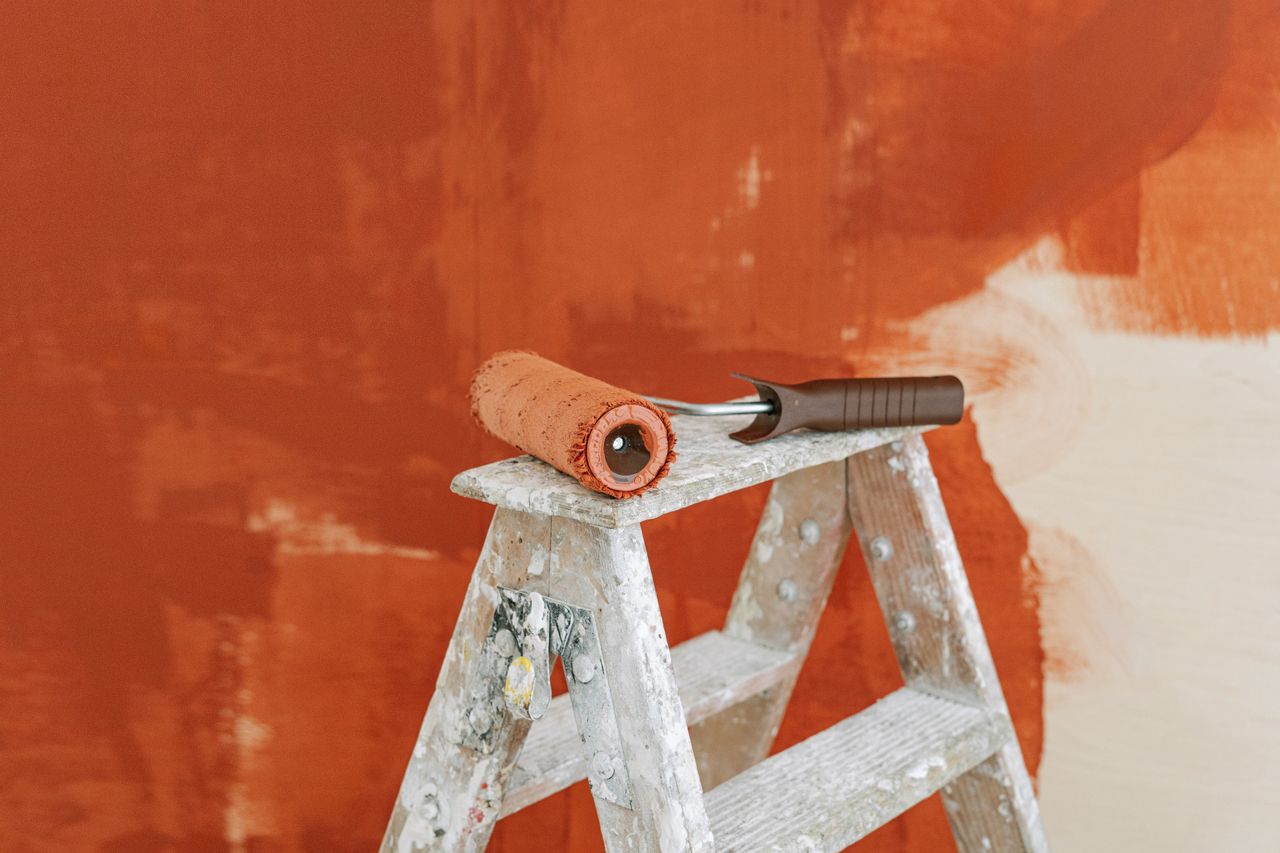 home-hero-1 Paint roller on a ladder with a partially painted red wall in the background.
