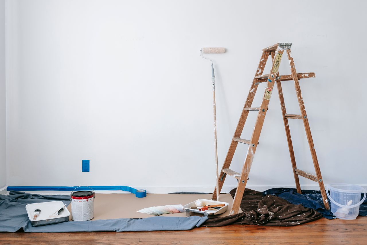 services-01 A room prepared for renovation with a ladder, paint supplies, and drop cloth.
